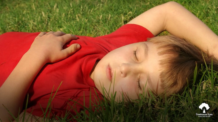 Child sleeping on grass outside.