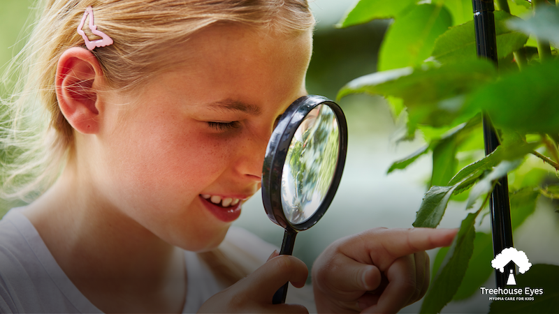 A young girl inspecting a leaf with a magnifying glass