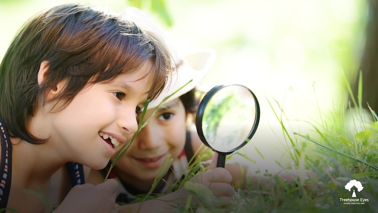Two kids looking through a magnifying glass outside.